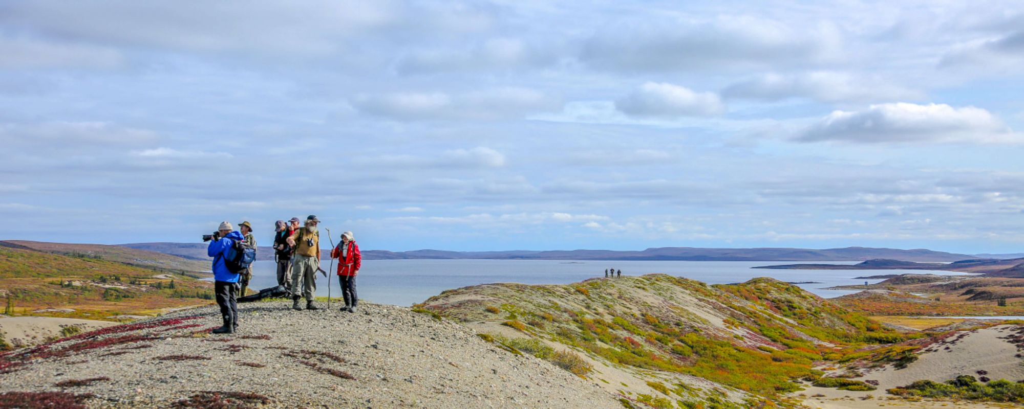 People on sand esker taking photos and over looking Point Lake and the barrens after hiking on a sand esker